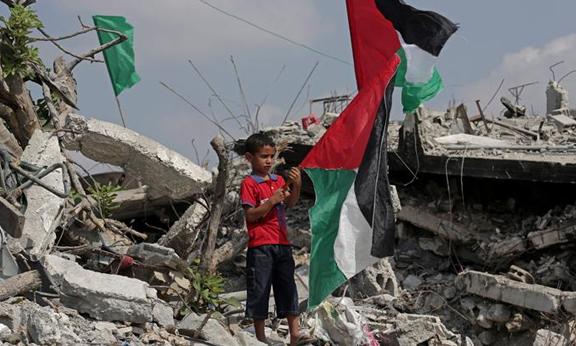 Palestinian boy holding flag on rubble of building