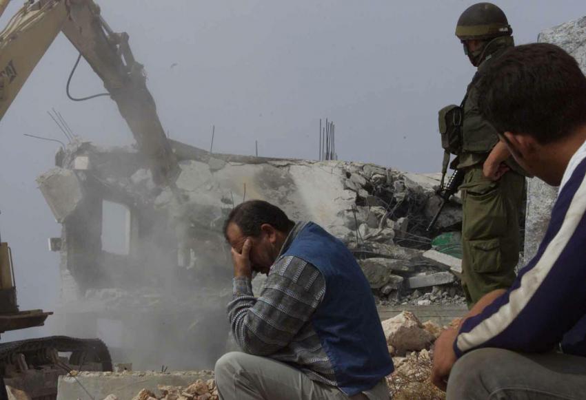 palestinian man with head in hands as a house is demolished in the background