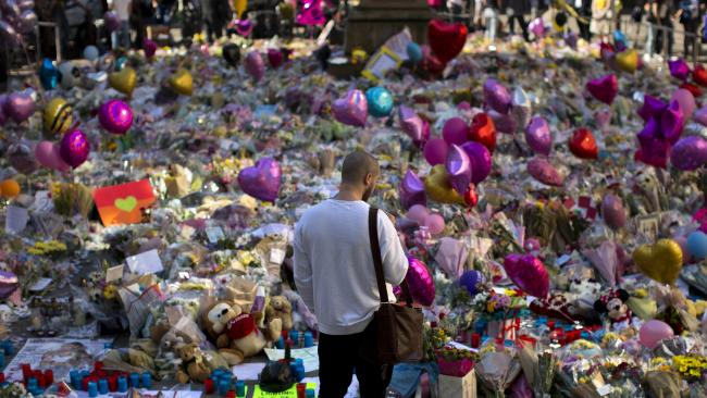 man standing in front of masses of floral tributes at Manchester