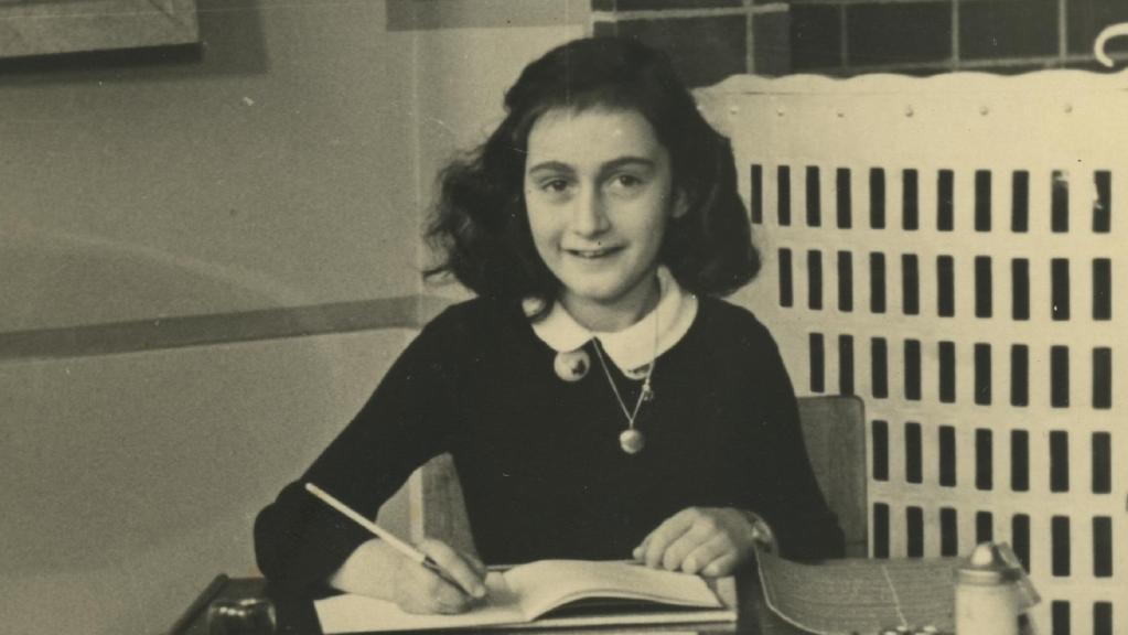 Anne smiling into the camera with open book and pencil in hand