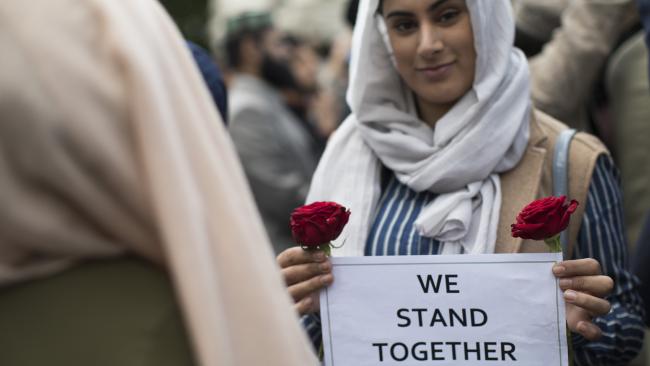 Muslim woman holding flowers and pro-peace sign at a rally smiling into the camera