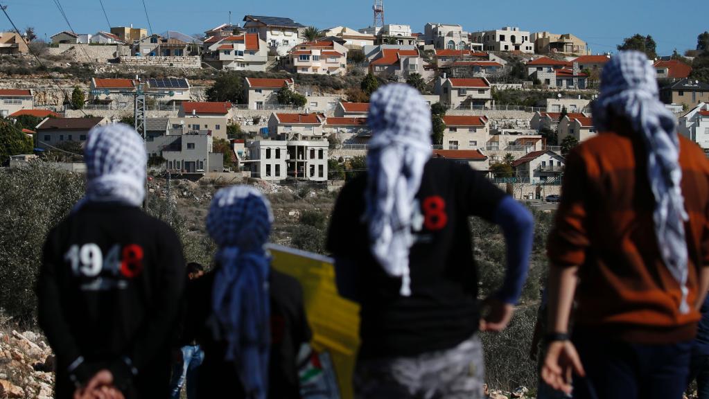 palestinian protesters in foreground facing an israeli settlement in the distance