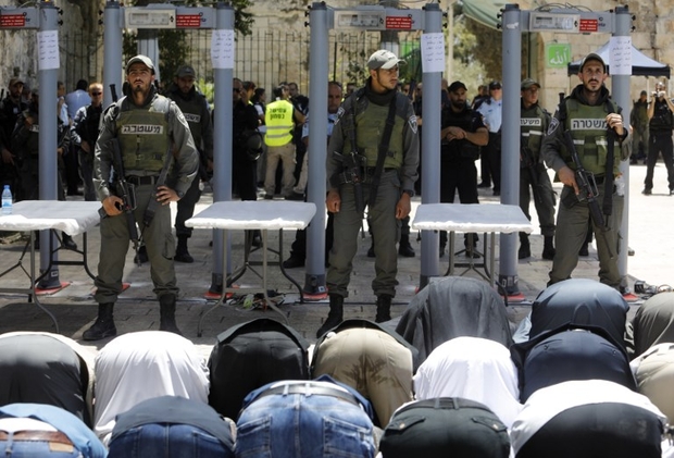 foreground muslim worshippers kneeling and in the background Israeli police officers next to metal detectors