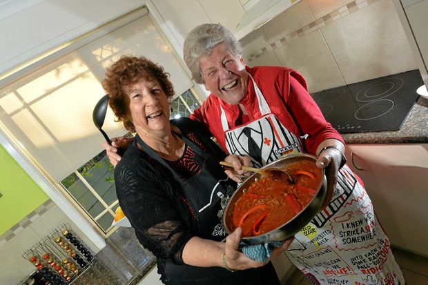 the two women holding the dish in the kitchen together smiling