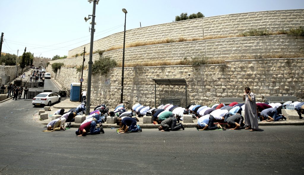 street corner with old city walls behind, and many moslems on floor praying