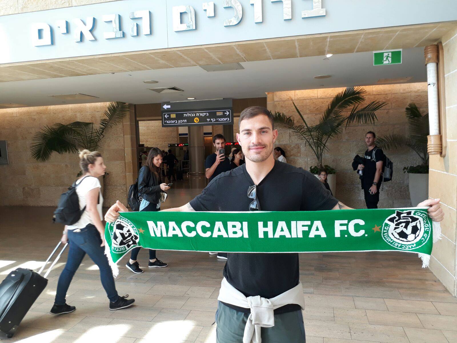 Troisi arriving at Ben Gurion airport holding up a Maccabi Haifa scarf