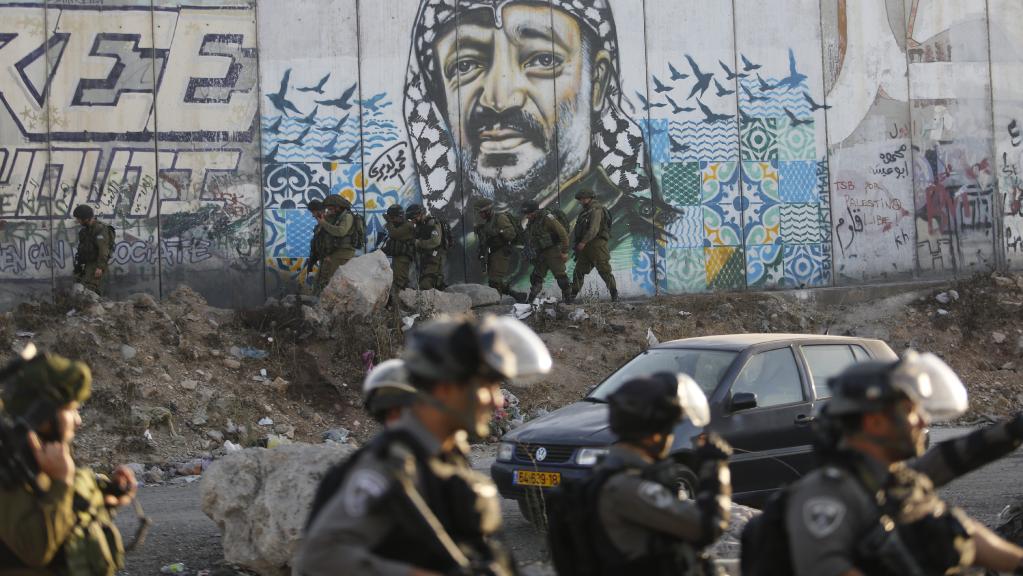 Israeli soldiers in front of separation wall with mural of arafat on it