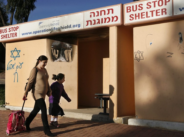 An Israeli mother passes by a bus stop which also serves as a bomb shelter as she accompanies her daughter to school in the Israeli southern city of Sderot
