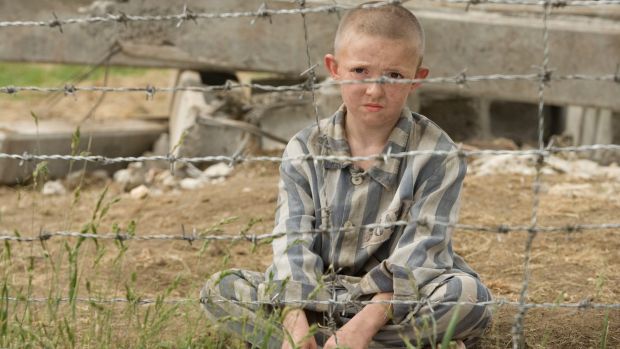 boy sitting in pyjamas behind barbed wire. still from movie