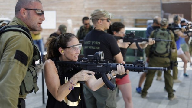 woman shooting a machine gun with instructors and others in background