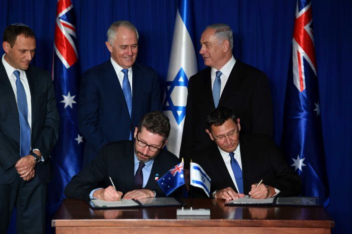 Prime Ministers Turnbull and Netanyahu standing behind others signing at a ceremony
