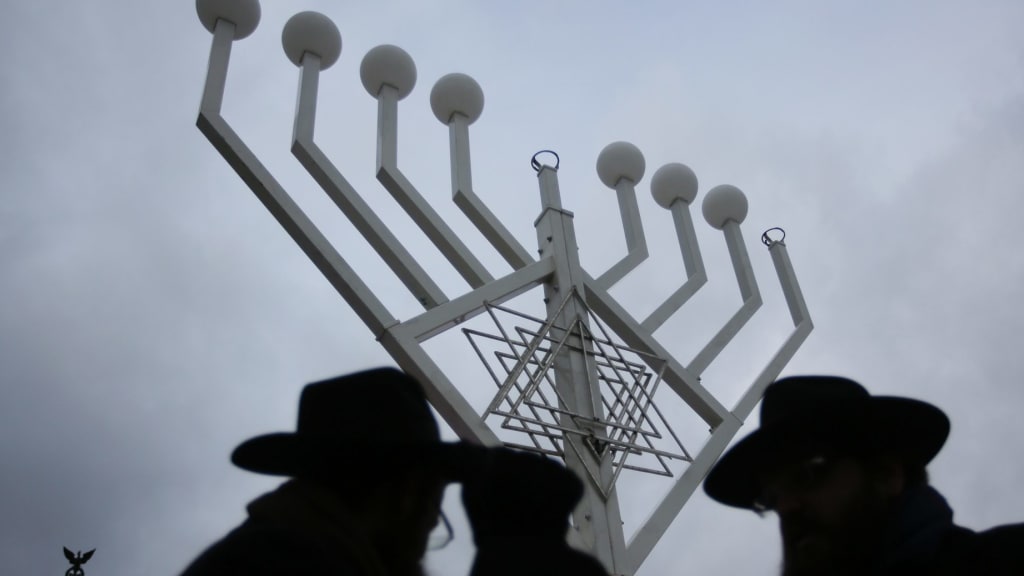 shot of a giant hanukkiah with the shadowed heads of three rabbis in the foreground