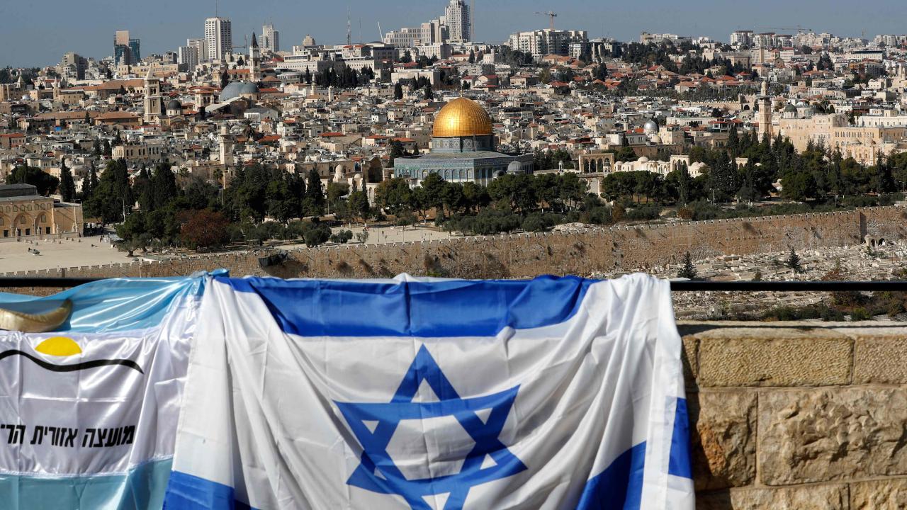 israeli flag draped over a wall with the dome of the rock in the background