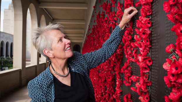 Judith with arm extended placing a flower in the wall that is filled with many poppies