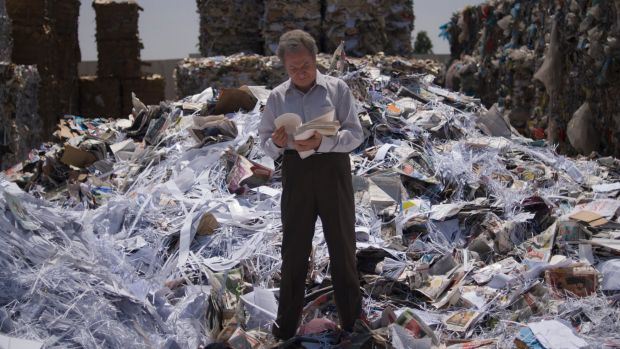 man flipping through papers standing on a mountain of rubbish/papers.