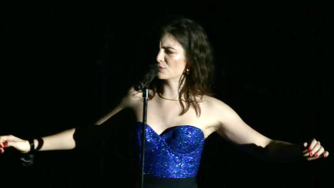 Lordeon stage in blue dress, arms spread, at the microphone