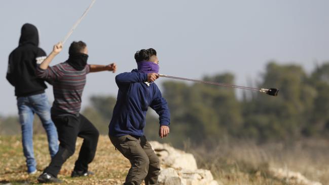 three masked protesters firing slingshots