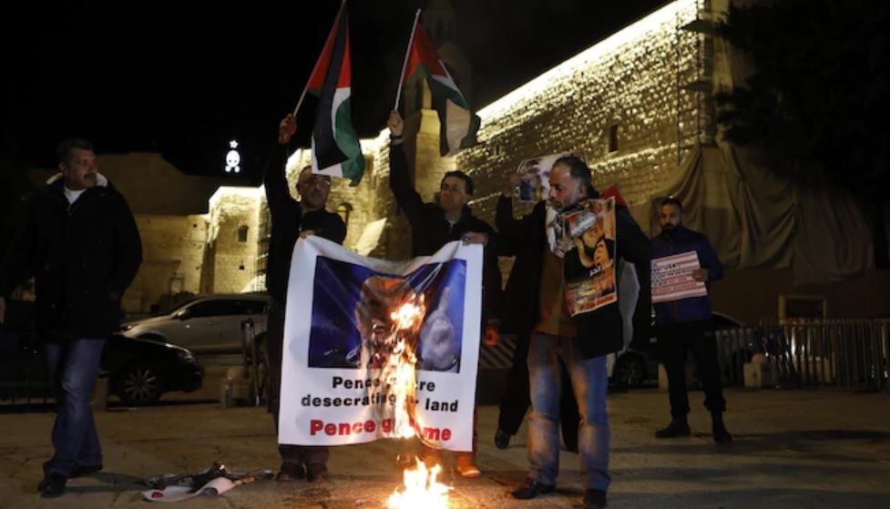 palestinian protesters in hte night outside old city walls burning a poster of Pence