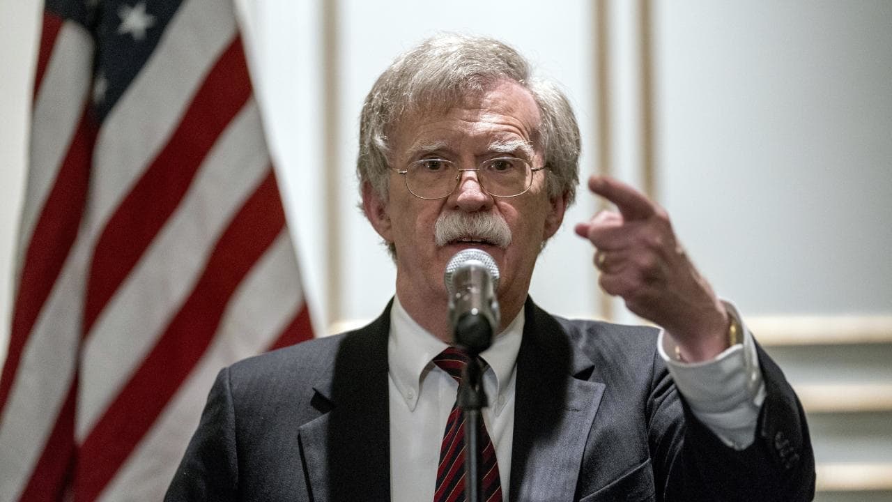 John Bolton at the microphone in front of American flag